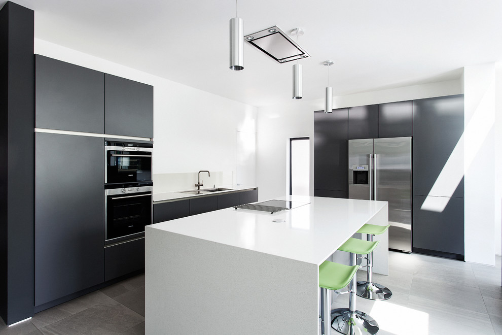 Medium sized contemporary u-shaped open plan kitchen in Hampshire with a double-bowl sink, flat-panel cabinets, brown cabinets, composite countertops, grey splashback, glass sheet splashback, stainless steel appliances, porcelain flooring and an island.