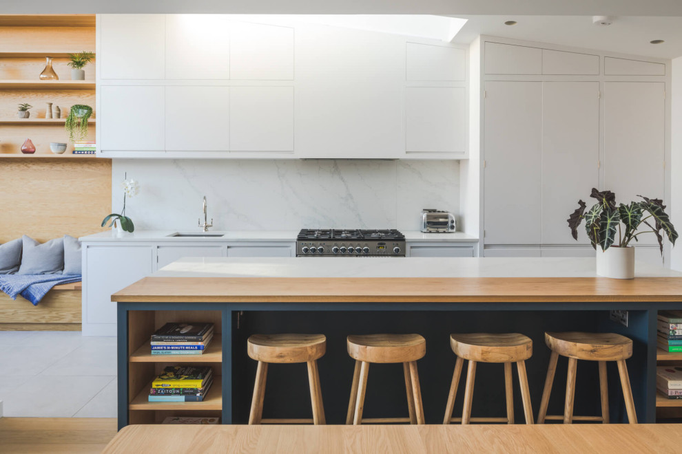 Design ideas for a large contemporary galley open plan kitchen in London with a built-in sink, flat-panel cabinets, white cabinets, quartz worktops, white splashback, stone slab splashback, ceramic flooring, an island, white floors, white worktops and integrated appliances.