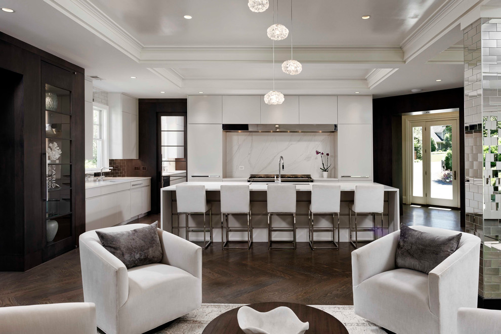 Modern inredning av ett vit vitt kök med öppen planlösning, med en undermonterad diskho, släta luckor, vita skåp, vitt stänkskydd, stänkskydd i sten, rostfria vitvaror, mörkt trägolv, en köksö och brunt golv