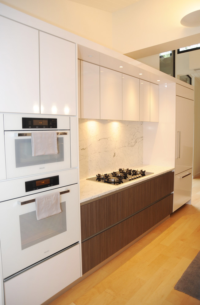 Photo of a large contemporary single-wall kitchen/diner in Philadelphia with a built-in sink, flat-panel cabinets, dark wood cabinets, marble worktops, white splashback, white appliances, light hardwood flooring, an island and stone slab splashback.