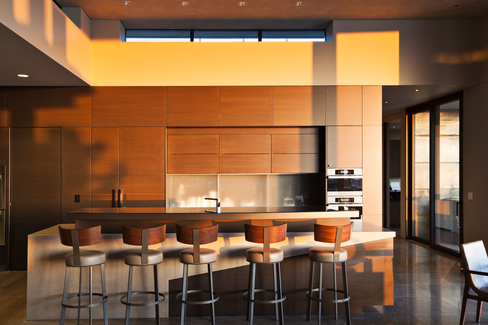 Cette photo montre une très grande cuisine ouverte parallèle et encastrable moderne en bois brun avec un placard à porte plane, un plan de travail en béton, une crédence grise, une crédence en carreau de verre, îlot et un sol en travertin.
