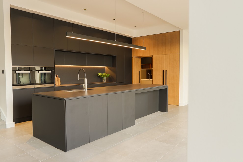 This is an example of a medium sized contemporary galley kitchen/diner in Sydney with a submerged sink, recessed-panel cabinets, black cabinets, engineered stone countertops, black splashback, stone slab splashback, stainless steel appliances, cement flooring, an island, grey floors and black worktops.