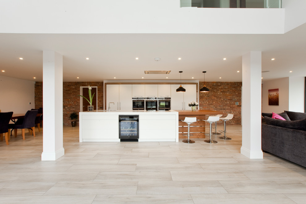 Photo of a large contemporary galley open plan kitchen in Cheshire with a submerged sink, flat-panel cabinets, white cabinets, quartz worktops, stainless steel appliances, porcelain flooring and an island.