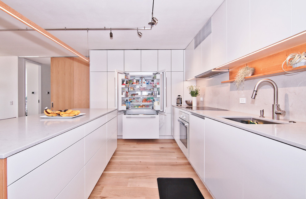Inspiration för mellanstora moderna kök, med en enkel diskho, släta luckor, vita skåp, bänkskiva i kvartsit, grått stänkskydd, stänkskydd i sten, integrerade vitvaror, ljust trägolv, en köksö och beiget golv