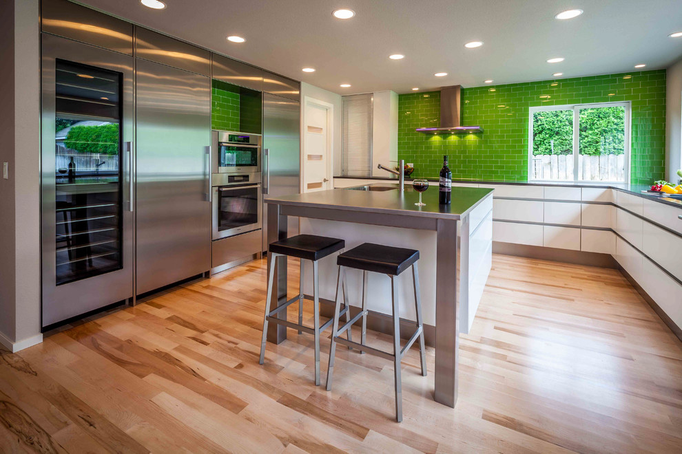 Large trendy u-shaped light wood floor and brown floor eat-in kitchen photo in Seattle with an undermount sink, flat-panel cabinets, white cabinets, quartz countertops, green backsplash, glass tile backsplash, stainless steel appliances and an island
