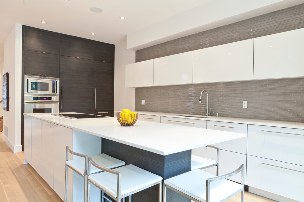 Bild på ett mellanstort funkis l-kök, med släta luckor, vita skåp, bänkskiva i kvartsit, grått stänkskydd, stänkskydd i mosaik, rostfria vitvaror, ljust trägolv och en köksö