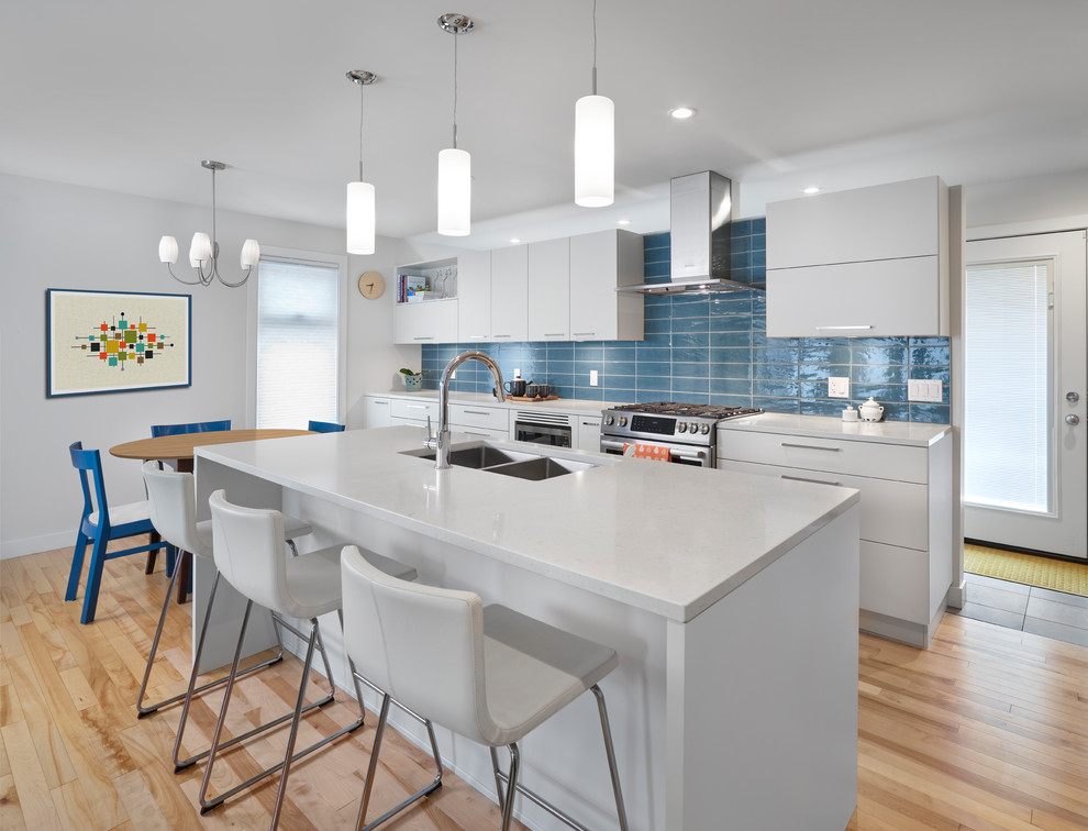 Photo of a medium sized scandi galley kitchen/diner in Edmonton with a submerged sink, flat-panel cabinets, grey cabinets, engineered stone countertops, blue splashback, metro tiled splashback, stainless steel appliances, light hardwood flooring and an island.