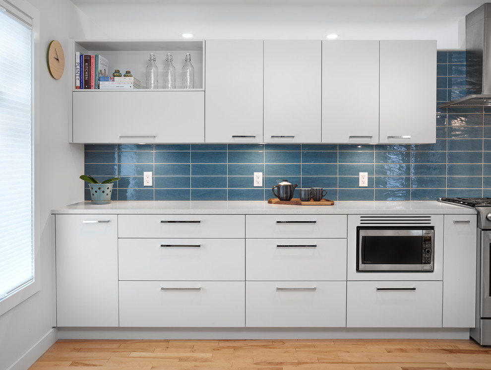 Bild på ett mellanstort nordiskt kök, med en undermonterad diskho, släta luckor, grå skåp, bänkskiva i kvarts, blått stänkskydd, stänkskydd i tunnelbanekakel, rostfria vitvaror, ljust trägolv och en köksö