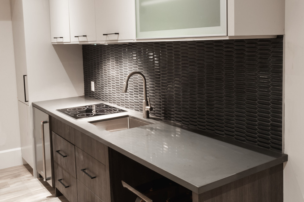 Bild på ett litet funkis grå linjärt grått kök med öppen planlösning, med en undermonterad diskho, släta luckor, grå skåp, bänkskiva i kvarts, svart stänkskydd, stänkskydd i keramik, rostfria vitvaror och flerfärgat golv