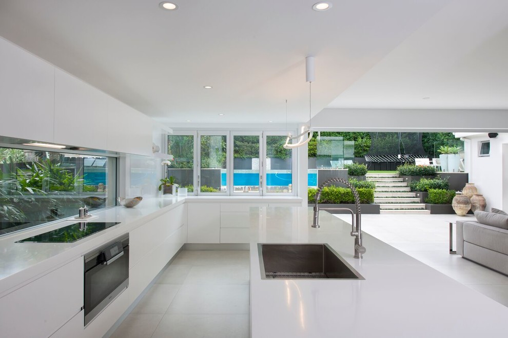 Photo of a medium sized contemporary galley open plan kitchen in Sydney with a built-in sink, flat-panel cabinets, white cabinets, glass sheet splashback, stainless steel appliances, an island and beige floors.