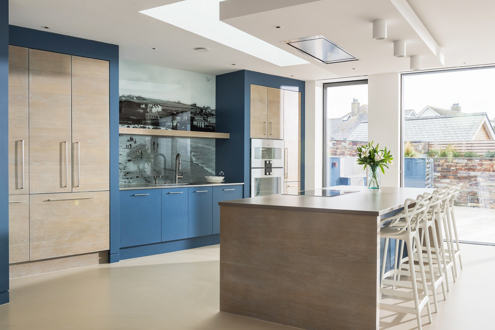 Große, Zweizeilige Moderne Küche mit flächenbündigen Schrankfronten, Quarzit-Arbeitsplatte, bunter Rückwand, Glasrückwand, Elektrogeräten mit Frontblende, Betonboden, Kücheninsel, beigem Boden, beiger Arbeitsplatte und blauen Schränken in Cornwall