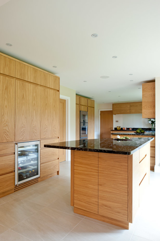 Photo of a large contemporary galley open plan kitchen in Kent with flat-panel cabinets, medium wood cabinets, granite worktops, black splashback, stone slab splashback, stainless steel appliances, limestone flooring and multiple islands.