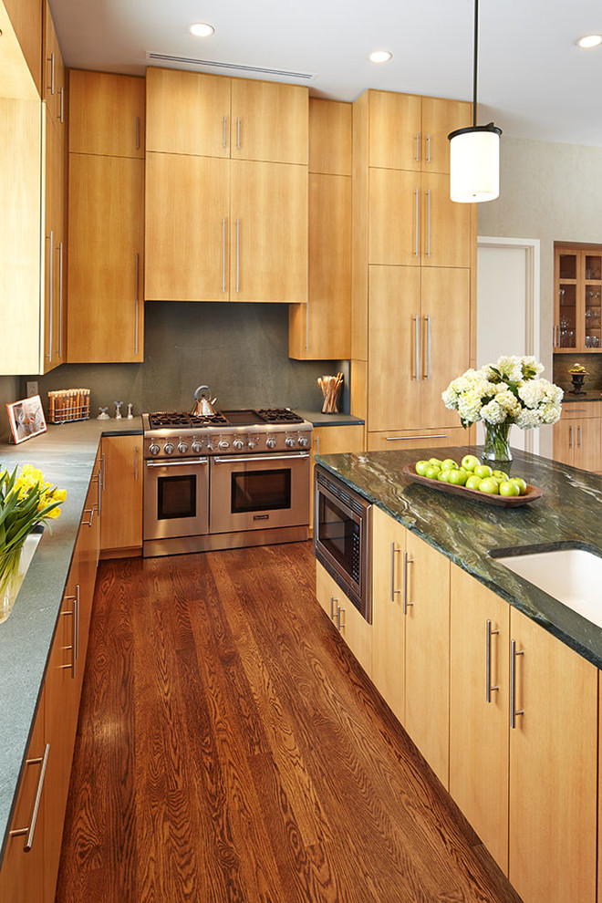 Cette image montre une cuisine ouverte design en U et bois clair de taille moyenne avec un placard à porte plane, îlot, un évier encastré, un électroménager en acier inoxydable, un sol en bois brun, un sol marron et un plan de travail vert.