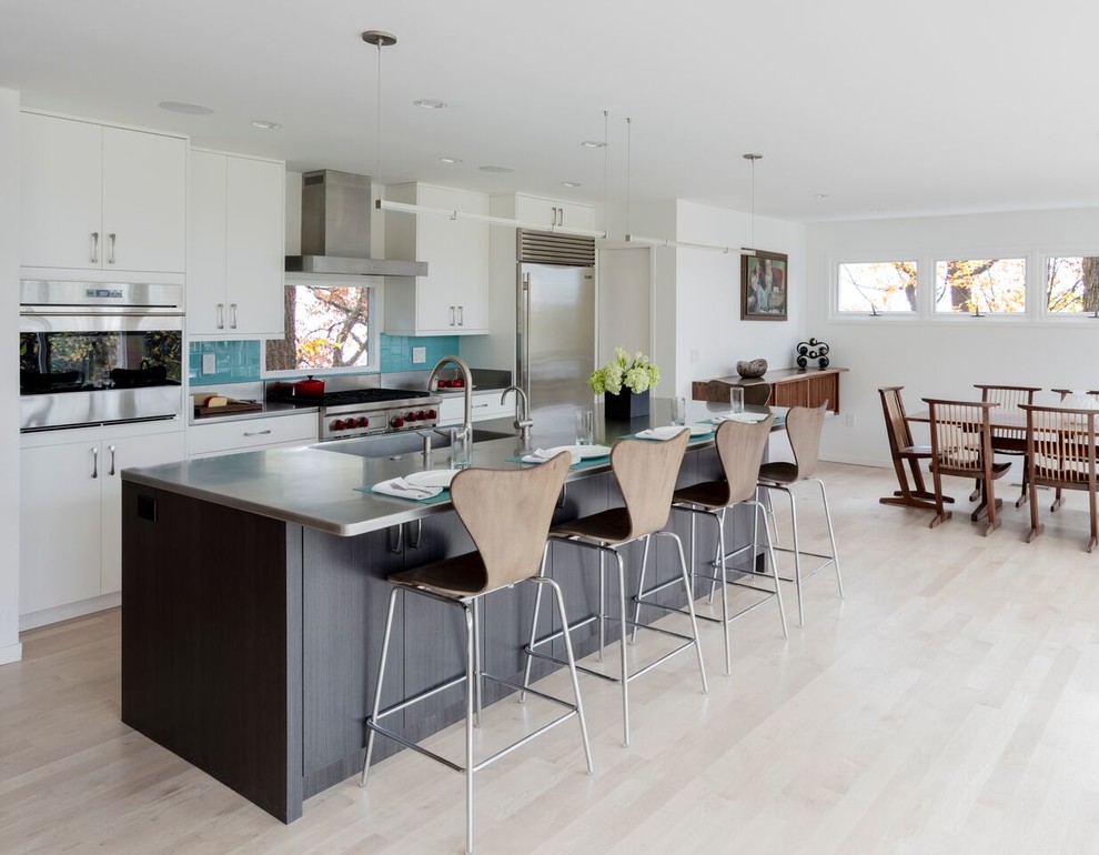 Example of a trendy single-wall light wood floor open concept kitchen design in DC Metro with a farmhouse sink, flat-panel cabinets, white cabinets, stainless steel countertops, blue backsplash, glass sheet backsplash, stainless steel appliances and an island