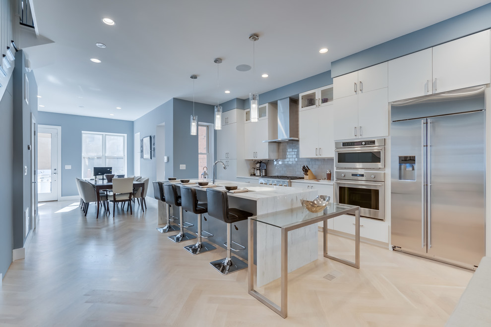 Mid-sized trendy galley light wood floor and beige floor open concept kitchen photo in DC Metro with an undermount sink, flat-panel cabinets, white cabinets, quartz countertops, white backsplash, glass tile backsplash, stainless steel appliances, an island and white countertops
