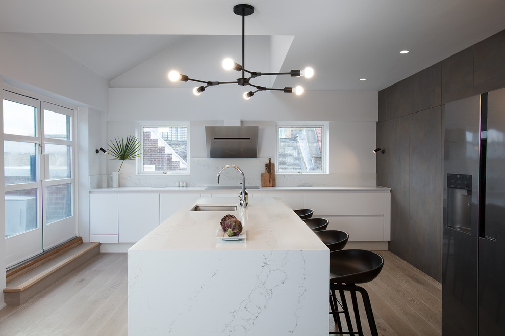 Design ideas for a contemporary u-shaped enclosed kitchen in London with a submerged sink, flat-panel cabinets, white cabinets, marble worktops, white splashback, marble splashback, integrated appliances, light hardwood flooring, an island, beige floors and white worktops.