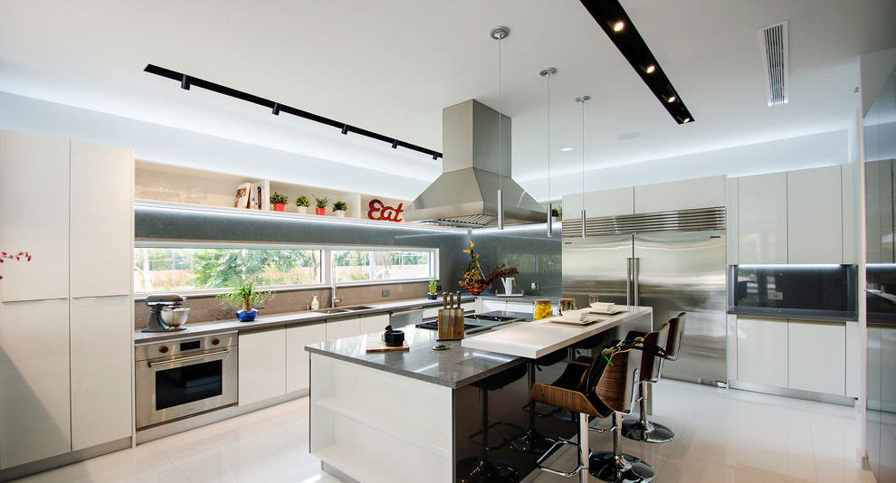 Large modern l-shaped enclosed kitchen in Miami with a double-bowl sink, flat-panel cabinets, white cabinets, engineered stone countertops, window splashback, stainless steel appliances, porcelain flooring, an island and white floors.