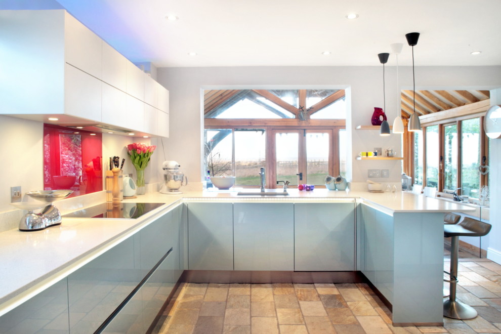 На фото: п-образная кухня среднего размера в современном стиле с обеденным столом, плоскими фасадами, синими фасадами, красным фартуком, фартуком из стеклянной плитки, техникой из нержавеющей стали и островом