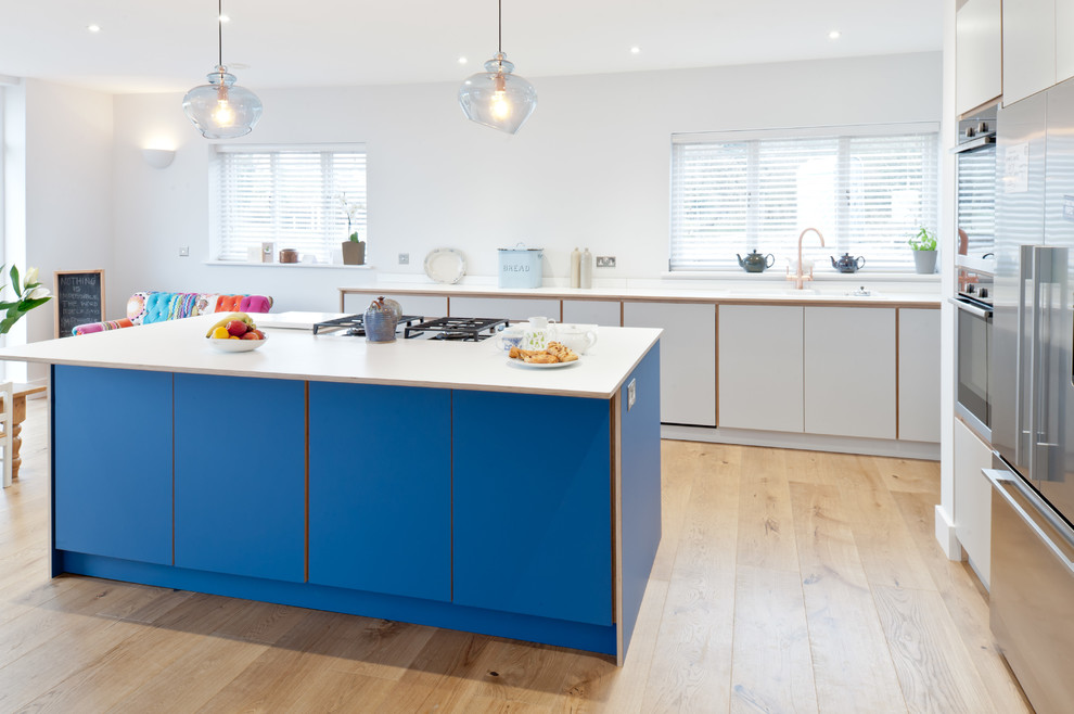Large contemporary galley open plan kitchen in Kent with flat-panel cabinets, laminate countertops, stainless steel appliances, light hardwood flooring, an island, brown floors, blue cabinets and white worktops.