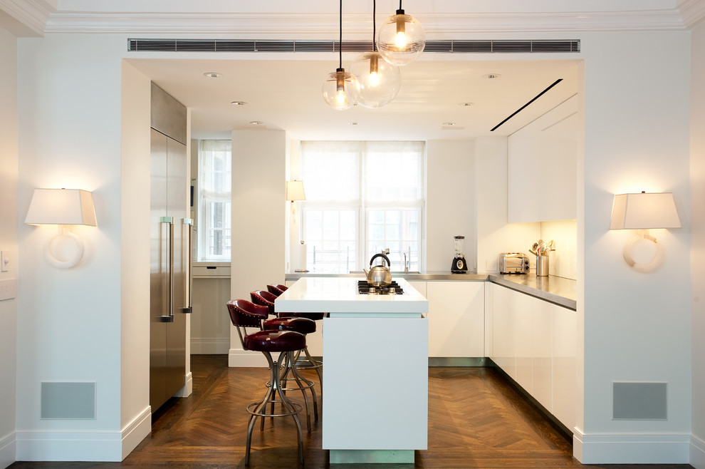 Modern inredning av ett stort l-kök, med en undermonterad diskho, släta luckor, vita skåp, glaspanel som stänkskydd, rostfria vitvaror, mellanmörkt trägolv och en köksö