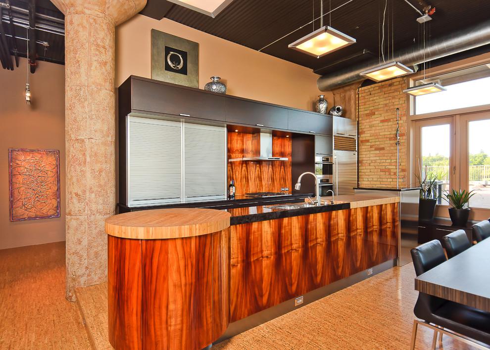 Einzeilige, Große Moderne Wohnküche mit flächenbündigen Schrankfronten, dunklen Holzschränken, Granit-Arbeitsplatte, Küchengeräten aus Edelstahl, Korkboden, Kücheninsel und Unterbauwaschbecken in Calgary