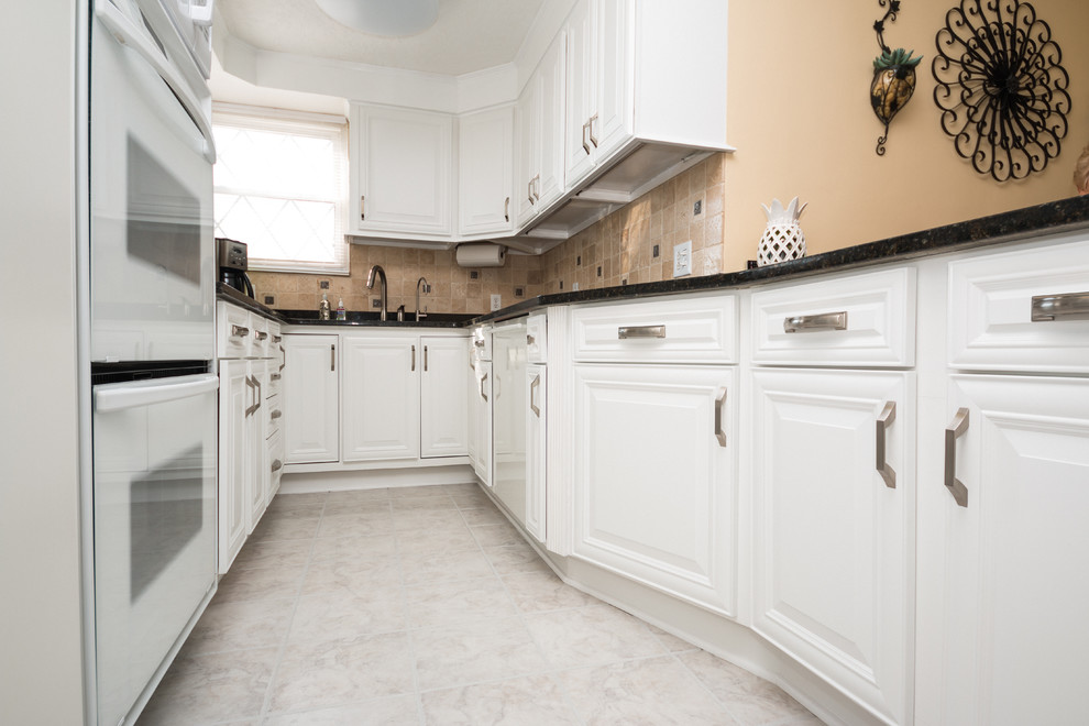 This is an example of a medium sized traditional galley kitchen/diner in Columbus with a submerged sink, raised-panel cabinets, white cabinets and white appliances.