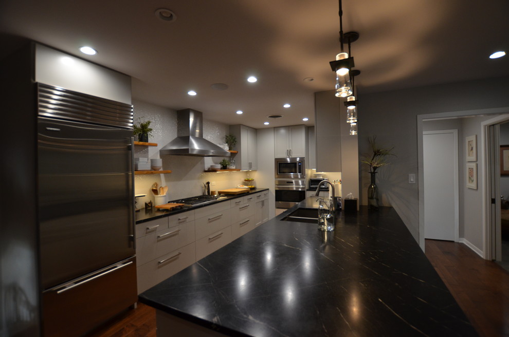 Modern inredning av ett stort kök, med en undermonterad diskho, släta luckor, grå skåp, bänkskiva i täljsten, vitt stänkskydd, stänkskydd i keramik, rostfria vitvaror, mellanmörkt trägolv och en köksö