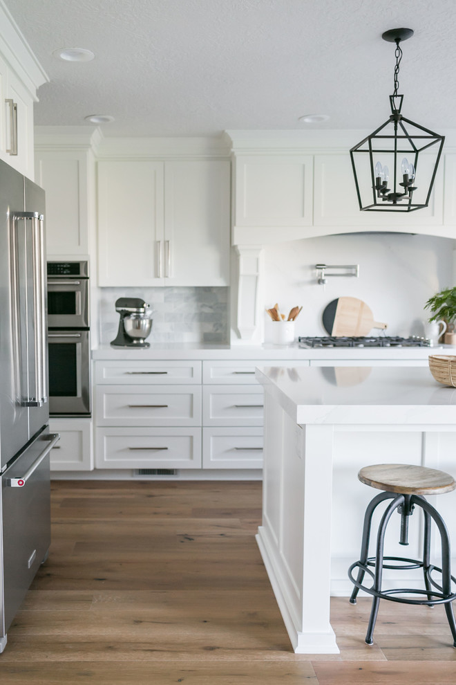 Foto på ett stort funkis vit linjärt kök och matrum, med en rustik diskho, luckor med infälld panel, vita skåp, bänkskiva i kvartsit, vitt stänkskydd, stänkskydd i travertin, rostfria vitvaror, ljust trägolv, en köksö och vitt golv
