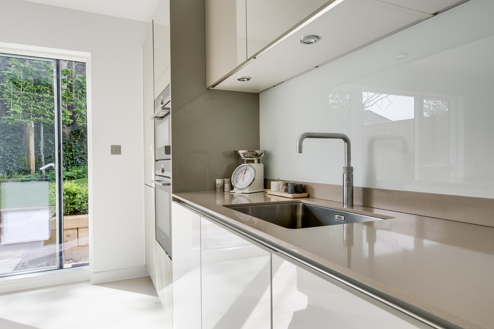 Immagine di una cucina contemporanea di medie dimensioni con lavello sottopiano, paraspruzzi con lastra di vetro, elettrodomestici da incasso e pavimento in gres porcellanato