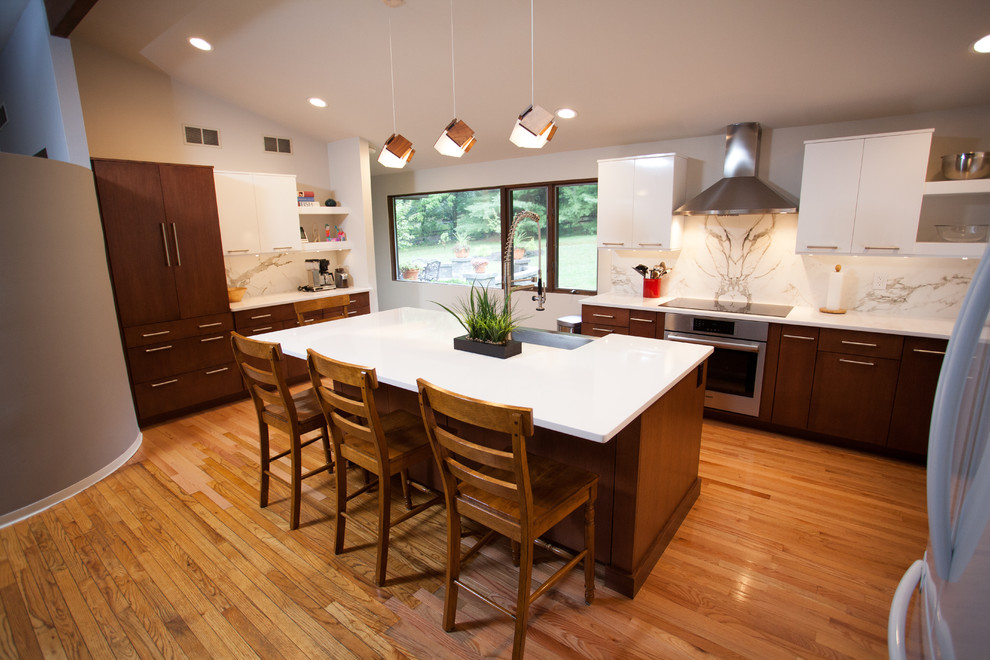 Example of a mid-sized trendy l-shaped light wood floor eat-in kitchen design in Philadelphia with a farmhouse sink, flat-panel cabinets, white cabinets, quartz countertops, white backsplash, stone slab backsplash, stainless steel appliances and an island