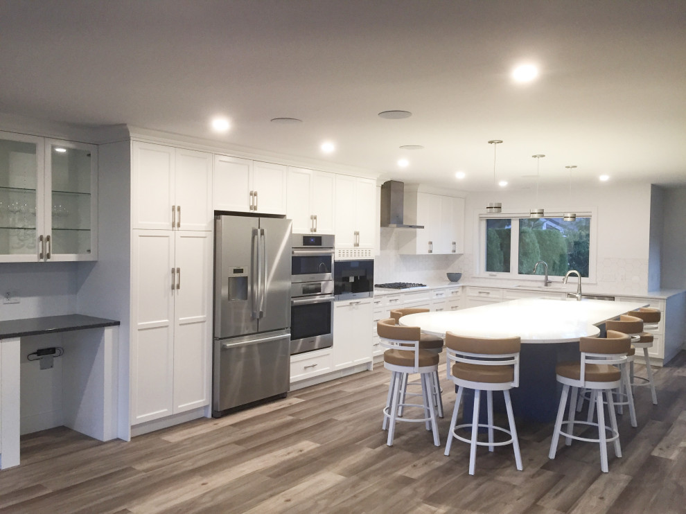 This is an example of a large contemporary l-shaped kitchen/diner in Vancouver with a submerged sink, flat-panel cabinets, white cabinets, engineered stone countertops, white splashback, ceramic splashback, stainless steel appliances, vinyl flooring, an island, brown floors and white worktops.