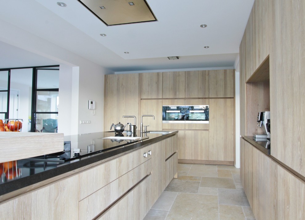 Foto på ett funkis kök och matrum, med en undermonterad diskho, släta luckor, skåp i mellenmörkt trä, granitbänkskiva, vitt stänkskydd, rostfria vitvaror, kalkstensgolv och en köksö