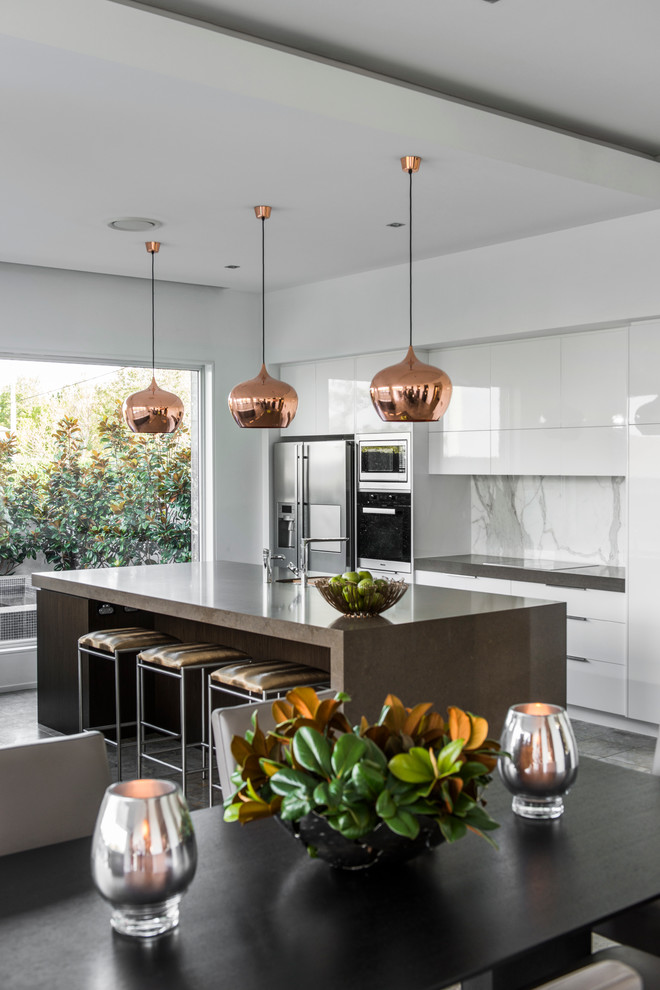 Inspiration for a contemporary galley kitchen in Brisbane with flat-panel cabinets, white cabinets, white splashback, stone slab splashback and stainless steel appliances.
