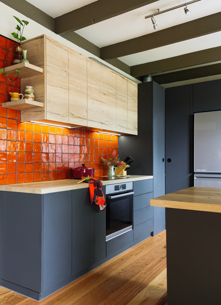 Foto på ett mellanstort funkis kök, med en dubbel diskho, släta luckor, laminatbänkskiva, orange stänkskydd, stänkskydd i keramik, svarta vitvaror, mellanmörkt trägolv och en halv köksö