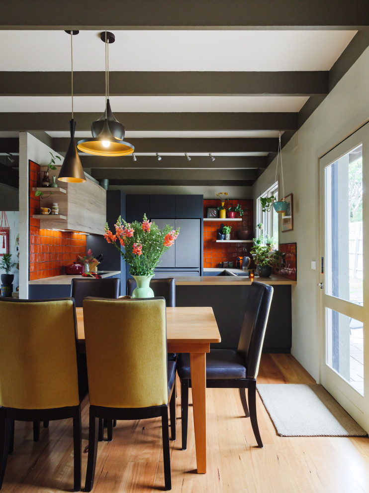 Modern inredning av ett kök, med en dubbel diskho, släta luckor, laminatbänkskiva, orange stänkskydd, stänkskydd i keramik, svarta vitvaror, mellanmörkt trägolv och en halv köksö