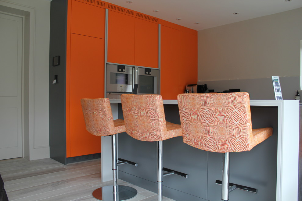 Свежая идея для дизайна: большая угловая кухня-гостиная в современном стиле с плоскими фасадами, оранжевыми фасадами, серым фартуком, фартуком из стекла, техникой из нержавеющей стали, полом из керамогранита и островом - отличное фото интерьера