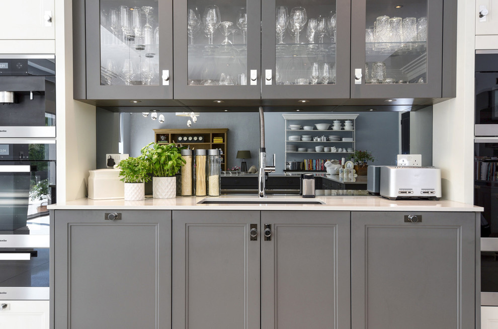 Foto di una grande cucina moderna con lavello da incasso, ante in stile shaker, ante grigie, top in granito, paraspruzzi grigio, paraspruzzi a specchio, elettrodomestici da incasso e top bianco