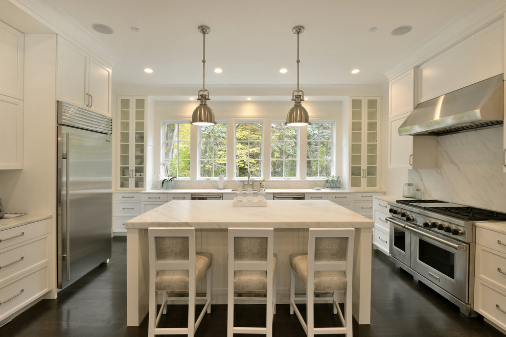 Exempel på ett stort klassiskt u-kök, med luckor med infälld panel, vita skåp, vitt stänkskydd, rostfria vitvaror och en köksö