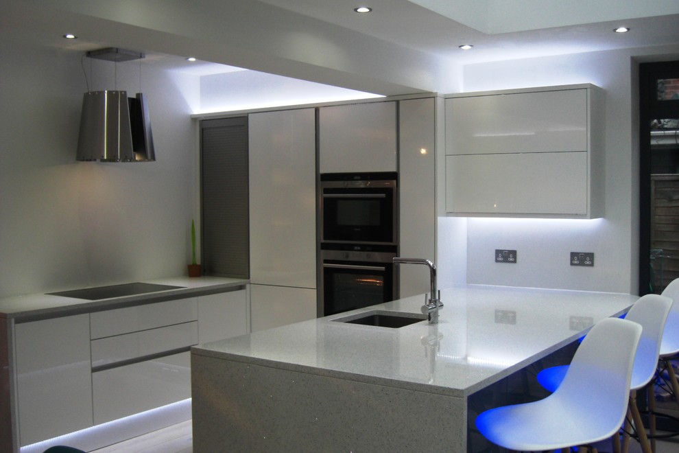 This is an example of a medium sized contemporary open plan kitchen in West Midlands with white cabinets and quartz worktops.