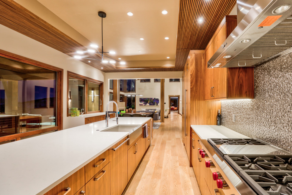 Foto di una grande cucina design con ante lisce, ante in legno scuro, paraspruzzi grigio, elettrodomestici da incasso, parquet chiaro e top bianco