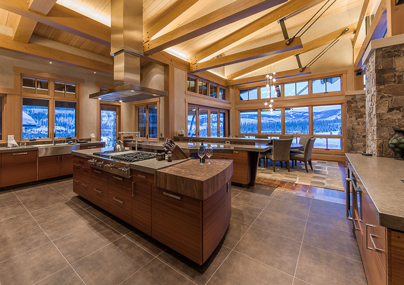 This is an example of a large contemporary l-shaped open plan kitchen in Denver with flat-panel cabinets, stainless steel appliances, a belfast sink, dark wood cabinets, limestone worktops, porcelain flooring, an island and brown floors.