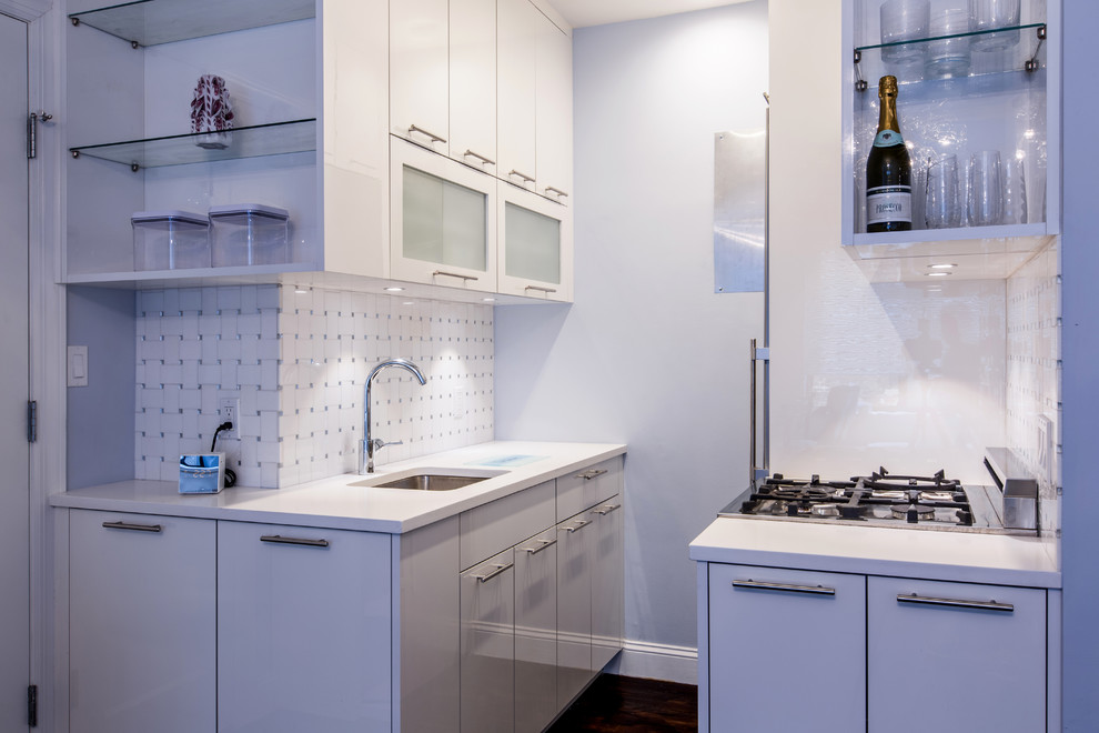 Small contemporary galley kitchen/diner in New York with a submerged sink, flat-panel cabinets, white cabinets, engineered stone countertops, white splashback, mosaic tiled splashback, stainless steel appliances and dark hardwood flooring.