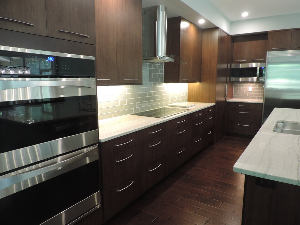 This is an example of a medium sized contemporary l-shaped open plan kitchen in Grand Rapids with a double-bowl sink, flat-panel cabinets, dark wood cabinets, quartz worktops, grey splashback, glass tiled splashback, stainless steel appliances, dark hardwood flooring and an island.
