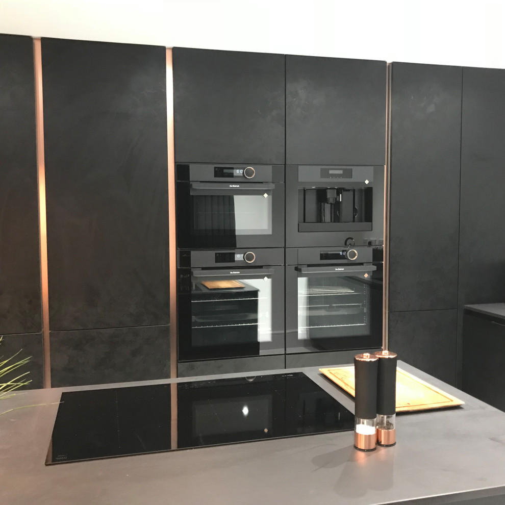 This is an example of a medium sized contemporary kitchen/diner in Cambridgeshire with an integrated sink, flat-panel cabinets, black cabinets, engineered stone countertops, black appliances, porcelain flooring, an island, white floors and black worktops.