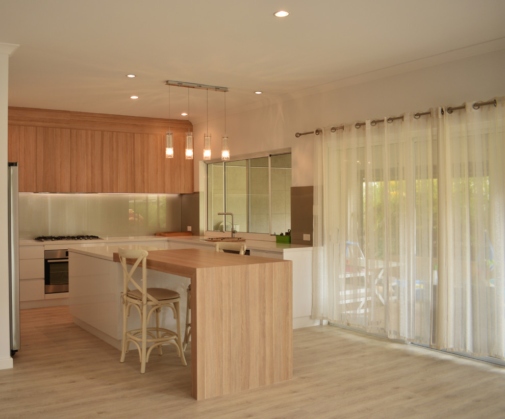 Exempel på ett stort modernt vit vitt kök, med en undermonterad diskho, släta luckor, skåp i mellenmörkt trä, granitbänkskiva, grått stänkskydd, glaspanel som stänkskydd, rostfria vitvaror, laminatgolv, flera köksöar och brunt golv