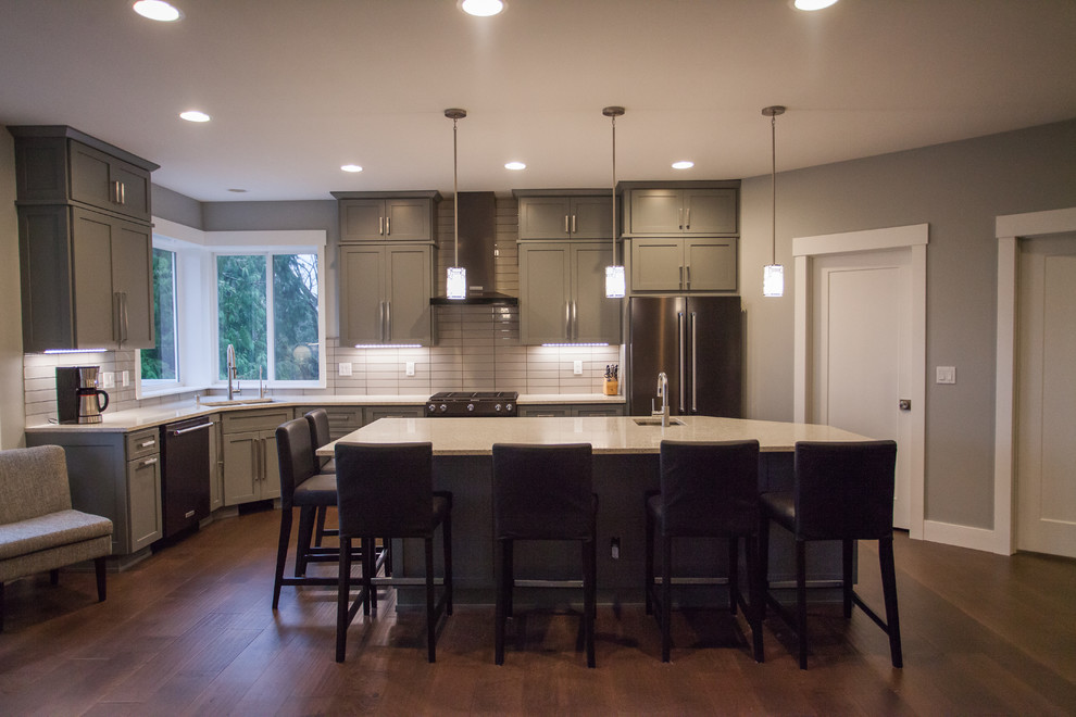 Example of a large trendy l-shaped brown floor and dark wood floor open concept kitchen design in Seattle with an undermount sink, shaker cabinets, gray cabinets, recycled glass countertops, gray backsplash, glass tile backsplash, stainless steel appliances and an island