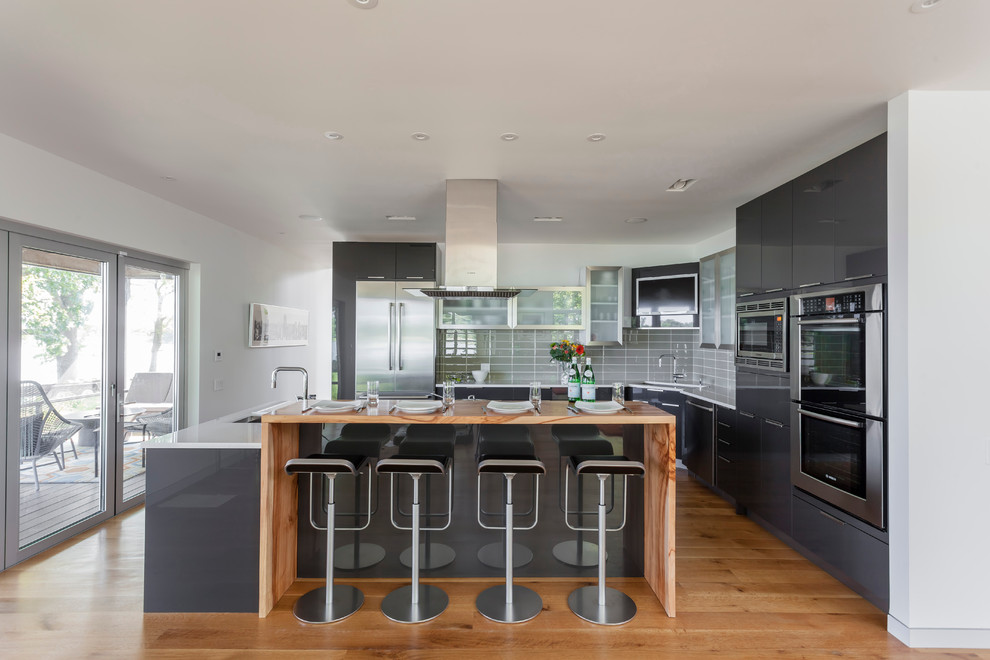 Foto di una cucina minimal di medie dimensioni con lavello sottopiano, ante lisce, ante grigie, paraspruzzi grigio, elettrodomestici in acciaio inossidabile e pavimento in legno massello medio