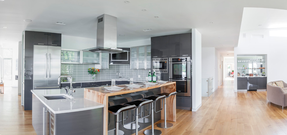 Modern inredning av ett mellanstort kök, med en undermonterad diskho, släta luckor, grå skåp, grått stänkskydd, stänkskydd i glaskakel, rostfria vitvaror, ljust trägolv och en köksö