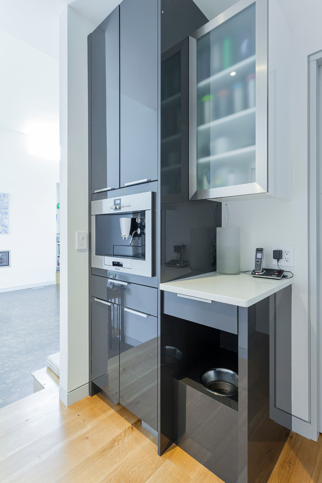 This is an example of a medium sized contemporary l-shaped open plan kitchen in Baltimore with a submerged sink, flat-panel cabinets, grey cabinets, grey splashback, glass tiled splashback, stainless steel appliances, light hardwood flooring and an island.