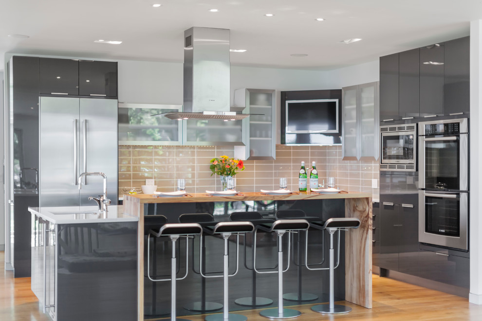 Medium sized contemporary l-shaped open plan kitchen in Baltimore with a submerged sink, flat-panel cabinets, grey cabinets, grey splashback, glass tiled splashback, stainless steel appliances, light hardwood flooring and an island.